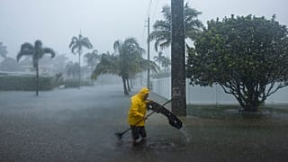 A man works to clear debris from a flooded street as heavy rain falls over parts of South Florida on Wednesday, June 12, 2024, in Hollywood, Fla.