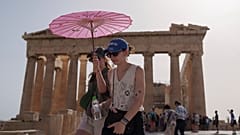 Touristen mit einem Regenschirm gehen vor dem Parthenon auf der antiken Akropolis im Zentrum Athens, Mittwoch, 12. Juni 2024. 