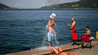 Menschen kühlen sich am Bosporus ab, während im Hintergrund an einem heißen Sommertag in Istanbul Rauch eines Waldbrands aufsteigt, 26. Juli 2023.