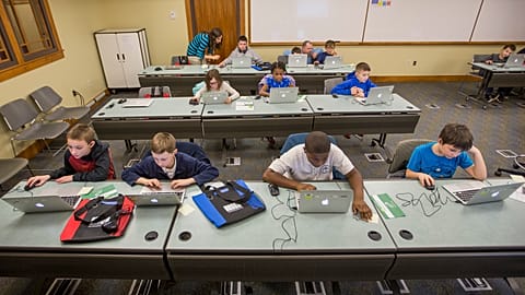 As crianças trabalham com computadores portáteis durante a aula.
