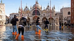 İnsanlar, 04 Aralık 2021 Cumartesi günü İtalya'nın Venedik kentinde, denizin gelgitiyle sular altında kalan San Marco Meydanı'ndan geçiyor. Su, deniz seviyesinden 99 santimetre yüksekliğe ulaştı ve şehrin en alçak kısımları