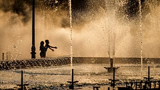 Des enfants profitent de la bruine d'une fontaine publique avant le coucher du soleil à Bucarest, Roumanie, jeudi 20 juin 2024.