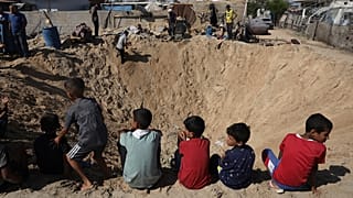 أطفال فلسطينيون يجلسون على حافة حفرة أحدثها انفجار إثر غارة جوية إسرائيلية في خان يونس.