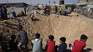 Des enfants palestiniens sont assis au bord d'un cratère après une frappe aérienne israélienne à Khan Younès, dans le sud de la bande de Gaza, le vendredi 21 juin 2024.