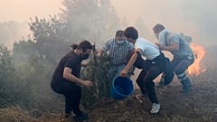 Κάτοικοι χρησιμοποιούν κουβάδες με νερό για να επιβραδύνουν τις φλόγες που πλησιάζουν τα σπίτια τους στο Alcabideche, έξω από τη Λισαβόνα, 25 Ιουλίου 2023.
