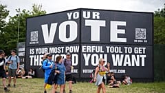 Festivalbesucher laufen während des Glastonbury-Festivals an einem Schild mit der Aufschrift "Your vote is your most powerful tool to get the world you want" vorbei. 