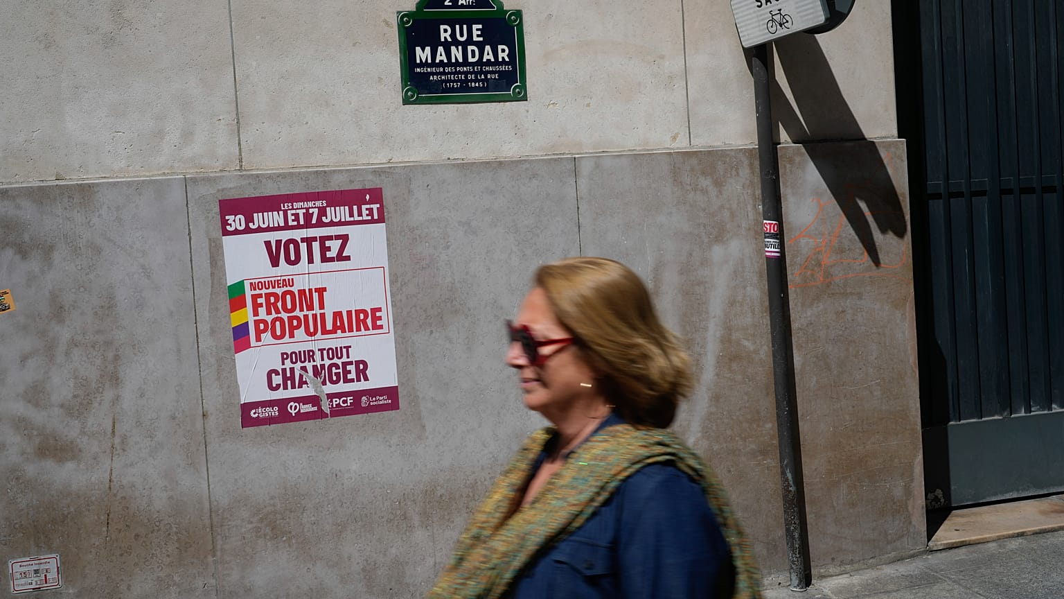Una mujer pasa junto a un cartel en el que se lee "Vota por el Nuevo Frente Popular" antes de las próximas elecciones parlamentarias en París.