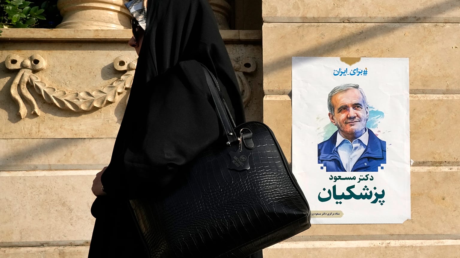 A woman walks past a poster of reformist candidate Masoud Pezeshkian in Tehran, June 29, 2024