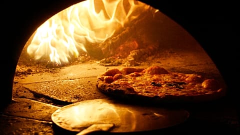 A pizza with a mozzarella cheese topping is cooked in a traditional wood fire oven in downtown Naples.