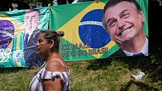 A woman walks past a banner featuring the Brazilian national flag and an image of former President Jair Bolsonaro.