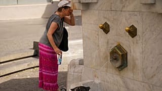 Una donna si rinfresca mentre un piccione beve acqua da una fontana pubblica a Belgrado, Serbia, 21 giugno 2024.