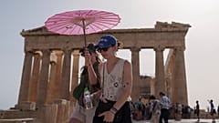 Touristen schützen sich vor der Hitze mit einem Spaziergang unter einem Regenschirm am Parthenon auf der antiken Akropolis im Zentrum Athens im Juni - dem heißesten Juni aller Zeiten