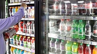 A shop owner reaches into a drink display refrigerator.