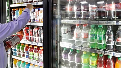A shop owner reaches into a drink display refrigerator.