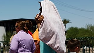 شخص يستخدم بطانية لحجب الشمس أثناء انتظاره لالتقاط صورة عند لافتة "مرحبًا بكم في لاس فيغاس" يوم الاثنين 8 يوليو 2024 