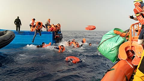 Rescue personnel of the SOS Mediterranee's volunteers, right, help transfer the passengers from a wooden migrant boat onto their own rescue vessel, on Tuesday, July 9, 2024. 