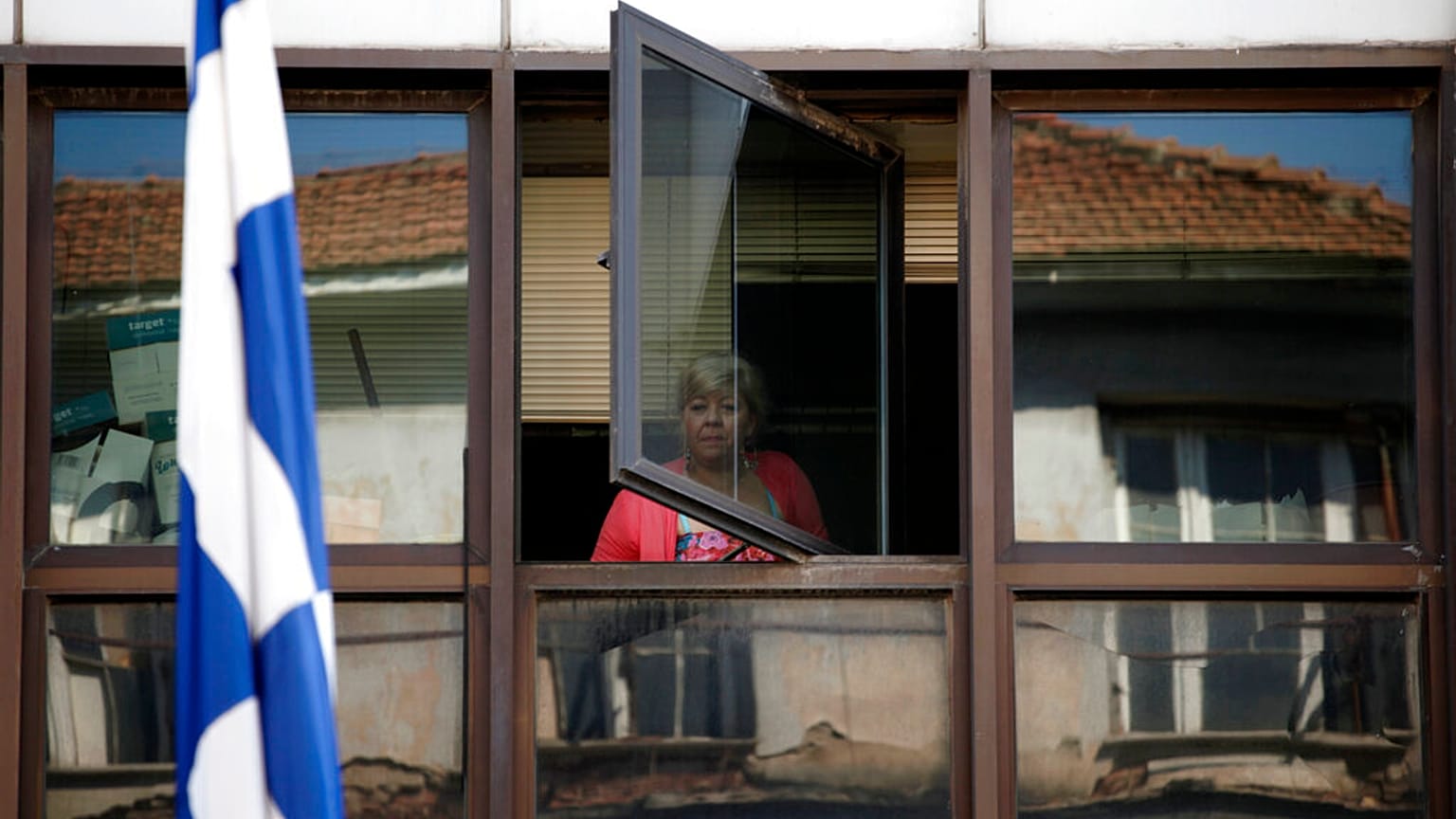 FILE - A municipal worker looks out a window of an occupied municipal building behind a Greek flag in central Athens, on Wednesday, July 10, 2013.
