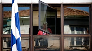 FILE - A municipal worker looks out a window of an occupied municipal building behind a Greek flag in central Athens, on Wednesday, July 10, 2013.