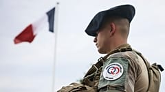 Um soldado junto à bandeira francesa no acampamento militar montado no bosque de Vincennes, segunda-feira, 15 de julho de 2024, nos arredores de Paris.