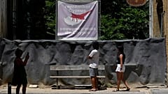 FILE -Tourist look at a road blocked with barrels and sand bags, with a banner showing the island in division at the top, 