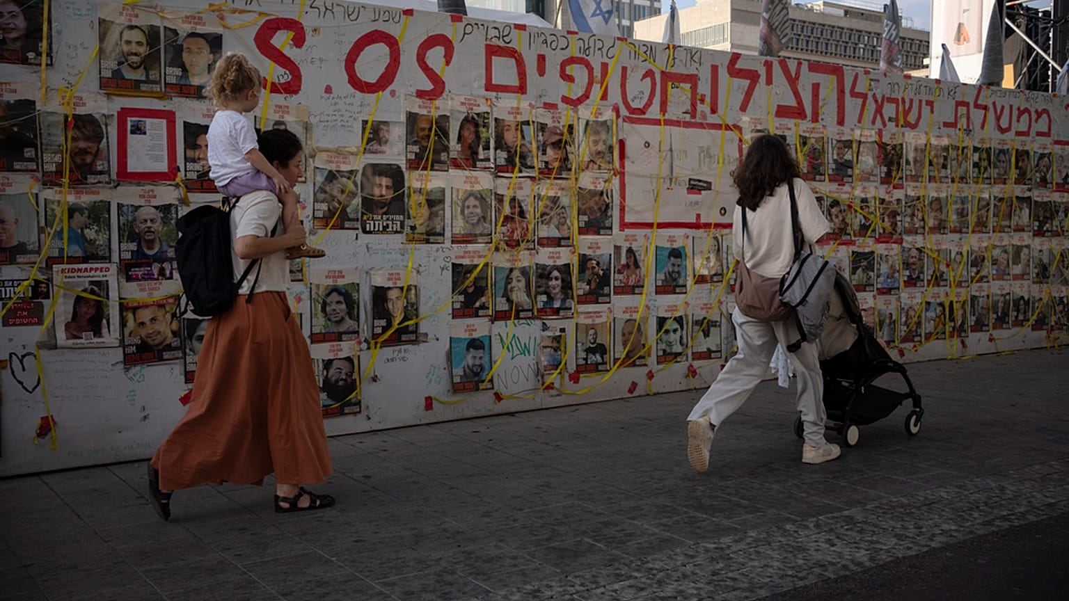 People walk past a wall with photos of hostages held in the Gaza Strip at a plaza known as Hostages Square in Tel Aviv, Israel