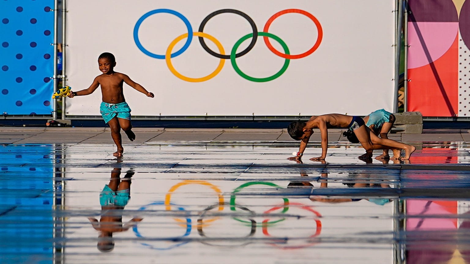 Children play at a splash fountain area near signage for the 2024 Summer Olympics, Tuesday, July 23, 2024, in Nice, France. Nice will host six soccer matches during the summer