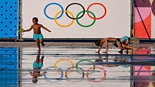 Children play at a splash fountain area near signage for the 2024 Summer Olympics, Tuesday, July 23, 2024, in Nice, France. Nice will host six soccer matches during the summer