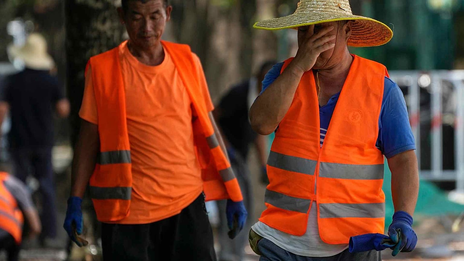 A worker wipes his sweat as he and his co-workers place tiles on a pavement on a sweltering day in Beijing, Monday, July 10, 2023.