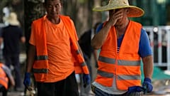 A worker wipes his sweat as he and his co-workers place tiles on a pavement on a sweltering day in Beijing, Monday, July 10, 2023.