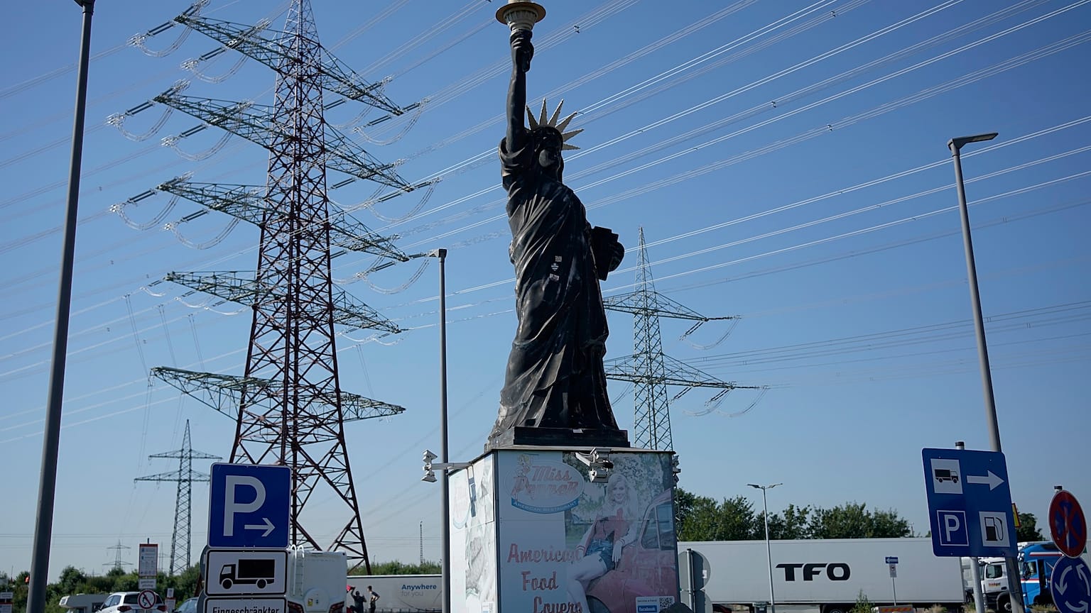 Köln yakınlarında kamyonların park ettiği bir benzin istasyonunda, özgürlük heykelinin bir replikasının arkasında yüksek gerilim direkleri duruyor 