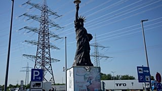 Köln yakınlarında kamyonların park ettiği bir benzin istasyonunda, özgürlük heykelinin bir replikasının arkasında yüksek gerilim direkleri duruyor 