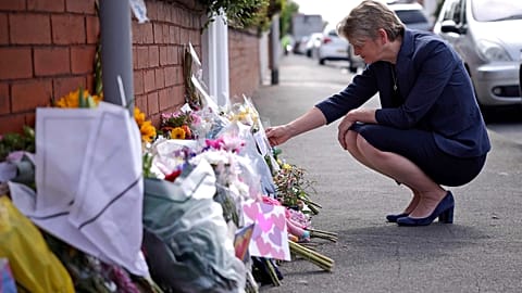 British Home Secretary Yvette Cooper looks at tributes near the scene in Hart Street where two children died and nine were injured in a knife attack.