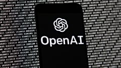 El logotipo de OpenAI aparece en un teléfono móvil frente a una pantalla de ordenador con datos binarios aleatorios.