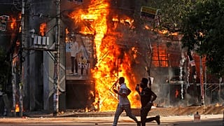 Des hommes passent devant un centre commercial incendié par des manifestants lors d'un rassemblement contre la Première ministre Sheikh Hasina, à Dhaka, dimanche 4 août 2024