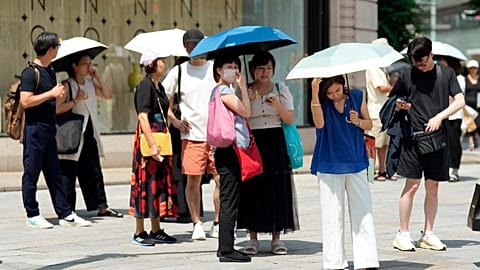 Pedestrian holding parasols stand under an intense sun at Ginza shopping street in Tokyo, on July 8, 2024.