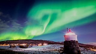 Aurora borealis or northern lights are visible in the sky above a lighthouse to the village of Strand near Tromso in northern Norway. 