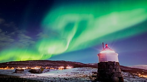 Aurora borealis or northern lights are visible in the sky above a lighthouse to the village of Strand near Tromso in northern Norway. 