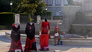 A couple relax by a fountain in front of a matador and traditional dress cutouts for tourists to pose behind for photos in Madrid, Spain, Friday, July 19, 2024.