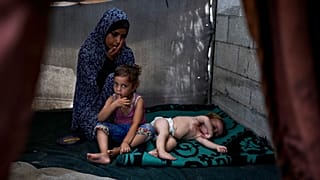 الفلسطينية منار الهيسي، التي نزحت بسبب القصف الإسرائيلي على قطاع غزة، تجلس بجوار أطفالها في مخيم مؤقت في دير البلح وسط قطاع غزة، الاثنين 29 يوليو 2024.