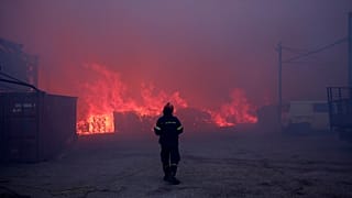 Un pompier se tient devant des bureaux en feu lors d'un incendie dans le nord d'Athènes, le lundi 12 août 2024,