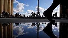 The Eiffel Tower is reflected in a puddle as people walk past at the Trocadero square, in Paris, France, Tuesday, Oct. 24, 2023. (AP Photo/Pavel Golovkin)