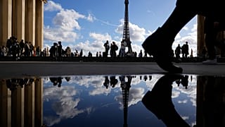 The Eiffel Tower is reflected in a puddle as people walk past at the Trocadero square, in Paris, France, Tuesday, Oct. 24, 2023. (AP Photo/Pavel Golovkin)