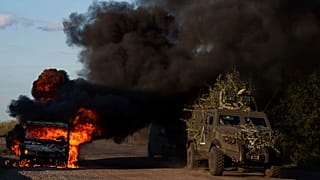 A Ukrainian armoured military vehicle travels past a burned car near the Russian-Ukrainian border in the Sumy region.