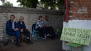Sudzha residents sit near a shelter with a sign that reads ‘Civilians in a basement. No military’, August 16, 2024