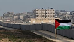ملف - يظهر العلم الفلسطيني على خلفية قسم من الجدار في ممر فيلادلفيا بين مصر وغزة، في الخلفية، بالقرب من مدينة رفح جنوب قطاع غزة، الأحد 1 يوليو/تموز 2007. (AP Photo/Khalil Hamr