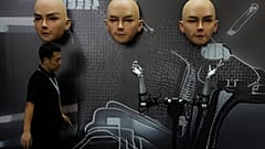 A worker walks past various kinds of human-like robots at the World Robot Conference held in Beijing.