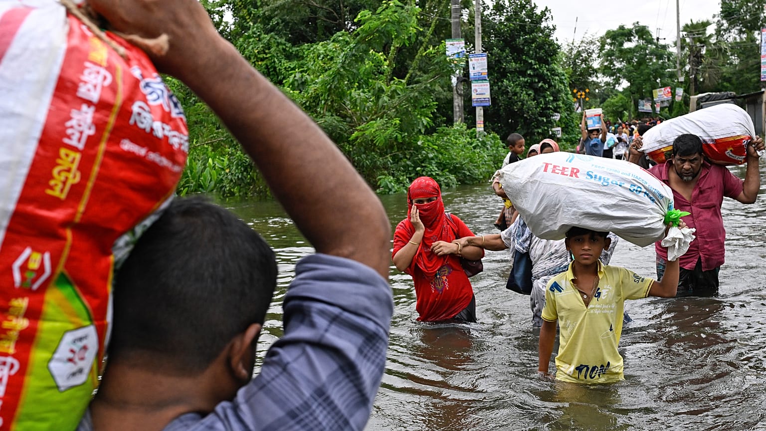 People walk to a relief shelter with belongings through a flooded street following heavy rains in Mohipal, Feni, a coastal district in southeast Bangladesh
