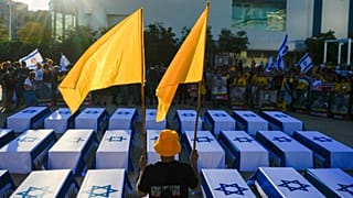 Bir adam, 27 rehineyi temsil eden İsrail bayraklarıyla kaplı sahte tabutların yanında bayrak tutuyor