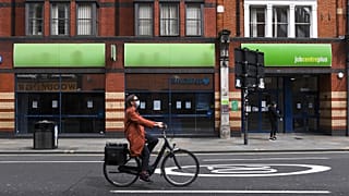 Bir kadın Londra'daki bir iş merkezinin önünden bisikletle geçiyor