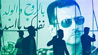 People walk in front of a campaign poster for Syrian President Bashar al-Assad with Arabic that reads: "In soul and child we redeem you al-Assad," May 2021